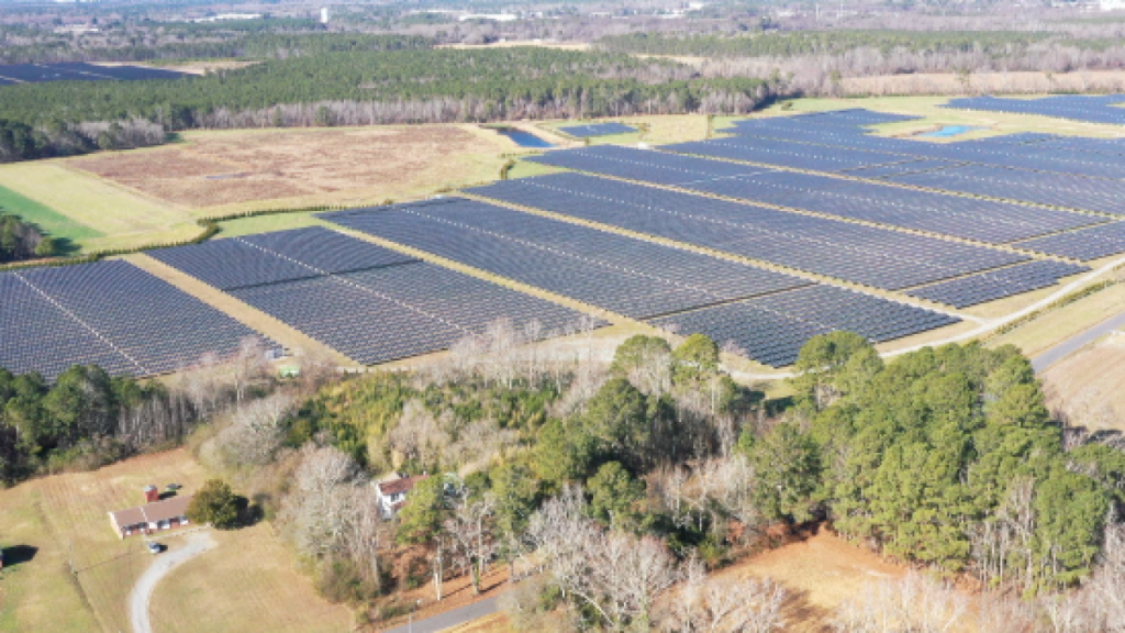 Aerial view of a large solar farm with numerous solar panels installed in Suffolk, Virginia, surrounded by agricultural land and trees.